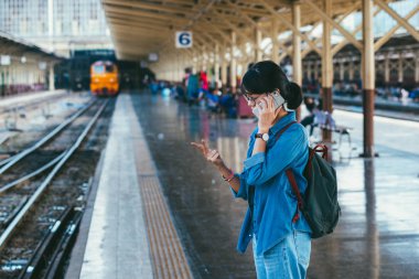 Asyalı kadın kullanılan gezgin akıllı telefon bekleyin ve onay zamanlama Tren İstasyonu - platform üzerinde tren iken parmak sayma ile seyahat ve ulaşım kavramı