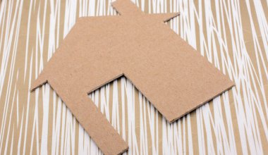 Tuvalin arka planında kağıttan yapılmış küçük bir ev şekli.