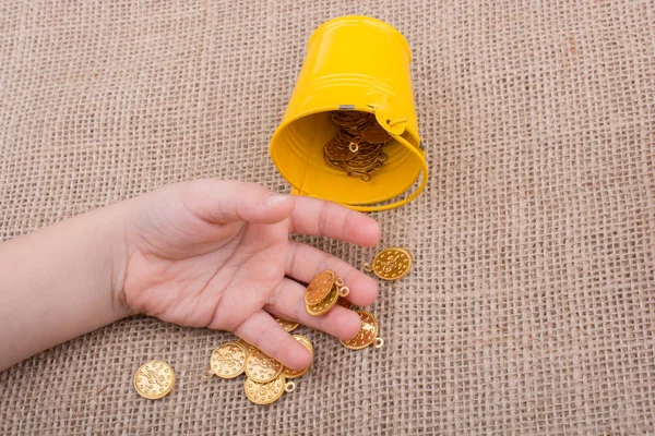 Bucket and fake gold coins in hand on canvas background