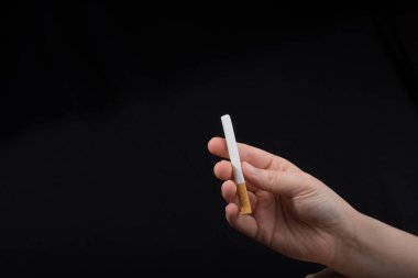 El siyah arka planda bir sigara tutuyor.