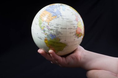 Üzerinde harita olan bir küreyi tutan el.