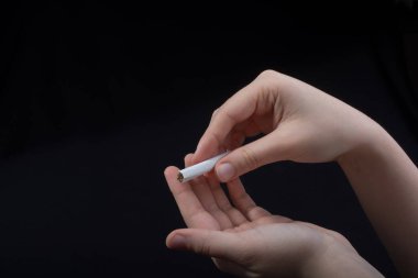 El siyah arka planda bir sigara tutuyor.