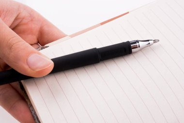 Beyaz zemin üzerine kalemle bir defter tutan el