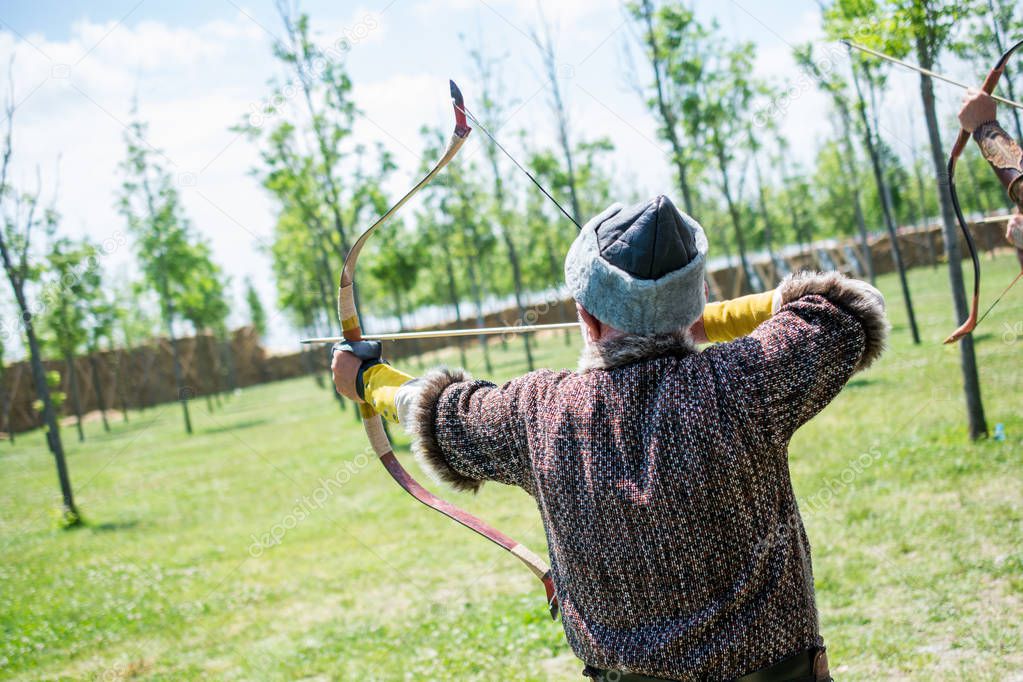 Archer with bow  in traditional clothes shooting an arrow