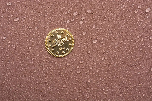 Fake gold coin covered with water drop in  close-up view