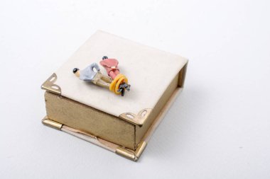 Küçük bir erkek figürü. Bir kitabın yanında ipe bağlanmış.