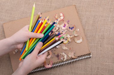 Bir defter kalem talaş ile üzerinde renkli kalemler tutan el