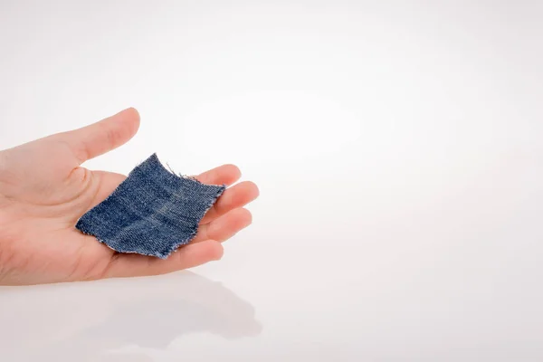 Hand holding a denim fabric piece on white background