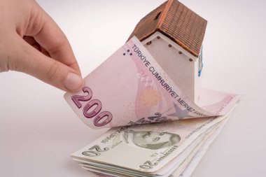 Beyaz arka planda, model evin yanında Türk Lirası banknotları el ele tutuşuyor