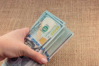 El ele tutuşan bir tomar Amerikan doları keten bir arka planda.