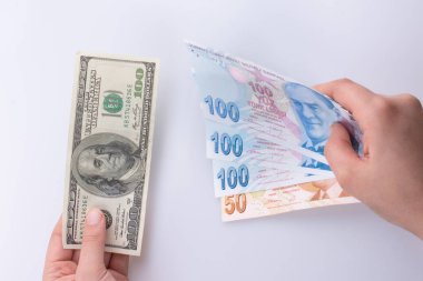 Beyaz arka planda Amerikan doları banknotları ve Türkçe Lira banknotları tutan kişi