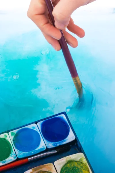 Paint dissolving in water as painting brush touching water