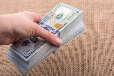 El ele tutuşan bir tomar Amerikan doları keten bir arka planda.