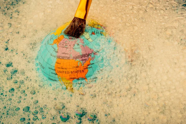 Paint brush placed on the top of globe in a water covered with foam