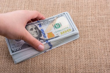 El ele tutuşan bir tomar Amerikan doları keten bir arka planda.