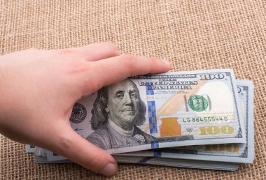 El ele tutuşan bir tomar Amerikan doları keten bir arka planda.
