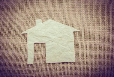 Tuvalin arka planında kağıttan yapılmış küçük bir ev şekli.