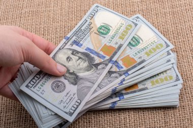 El ele tutuşan bir tomar Amerikan doları keten bir arka planda.