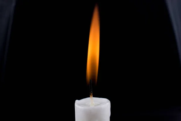 burning white candle on black background