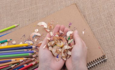 Elindeki renkli kalem talaşları bir deftere.