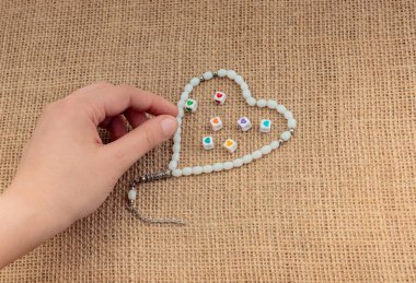 Elinde kalp şeklinde bir nesne, tuvalde dua eden boncuklarla.