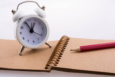 Renkli kalem ve bir kahverengi spiral defter üzerinde yerleştirilen bir çalar saat