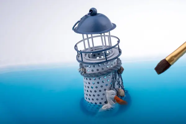 青い水に入れるブラシや小さなモデル灯台の塗装 — ストック写真