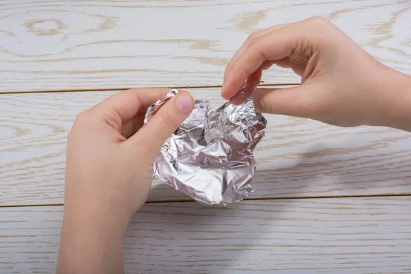 Tahta bir arka planda kalp şeklinde alüminyum folyo yırtılıyor.