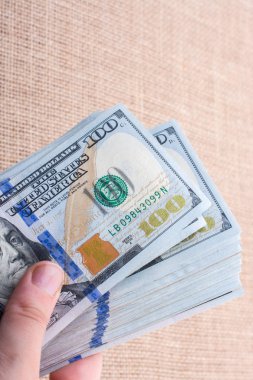 El ele tutuşan bir tomar Amerikan doları keten bir arka planda.