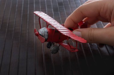 Ahşap bir dokuda kırmızı bir oyuncak uçak tutuyor.