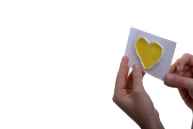 Beyaz arka planda kağıttan kesilmiş sarı bir kalp şeklindeki kağıdı tutan el.