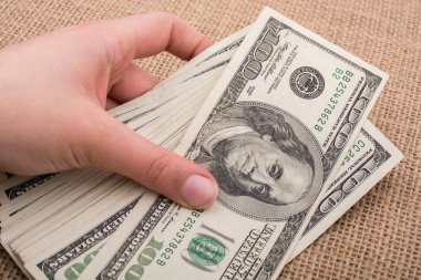 El ele tutuşan bir tomar Amerikan doları keten bir arka planda.