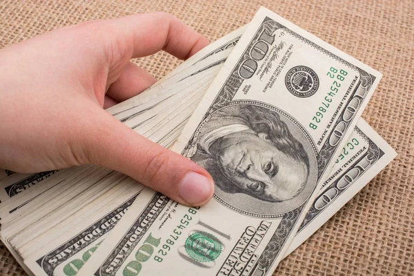 El ele tutuşan bir tomar Amerikan doları keten bir arka planda.