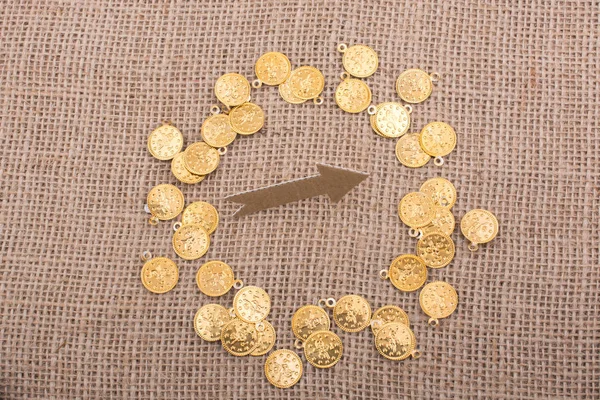 Fake gold coins around arrow shape made of paper
