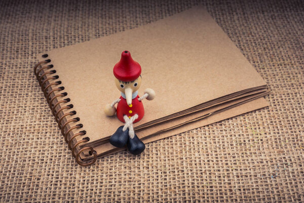 Pinocchio sitting on notebook on a canvas background