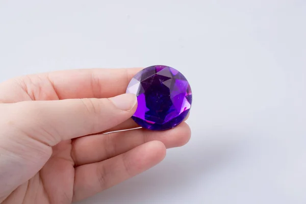 Mão segurando um diamante roxo no fundo branco — Fotografia de Stock