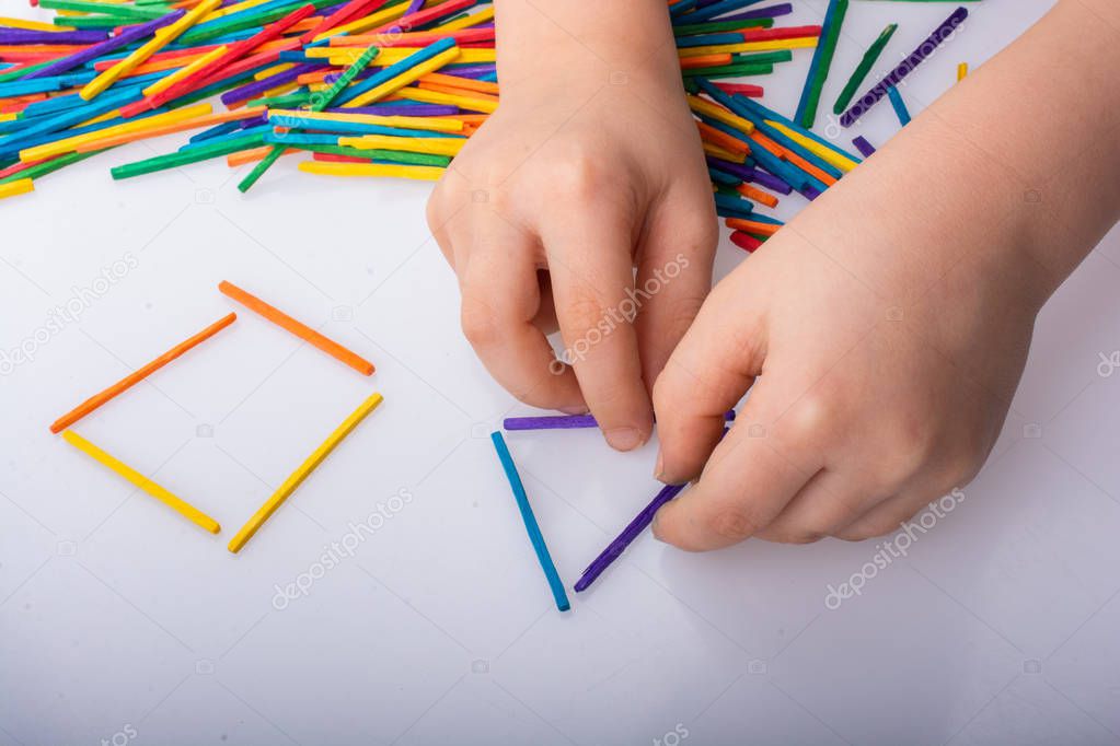 Kid making geometric shapes with colorful sticks on white backgr