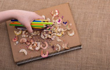 Renkli kalemler üzerinde bir defter tutan el