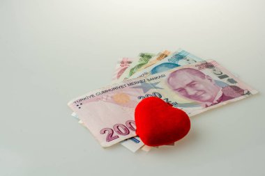 Türk Lirası, beyaz zemin üzerinde kırmızı renkli kalp şeklindeki nesnenin yanına para yatırıyor
