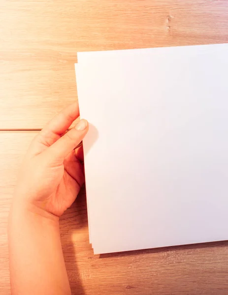 Mão segurando folhas de papel sobre fundo de madeira — Fotografia de Stock