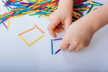 Çocuk beyaz backgr üzerinde renkli çubuklarla geometrik şekiller yapmak