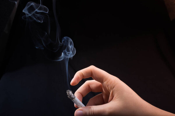 Рука держит сигарету на черном фоне
