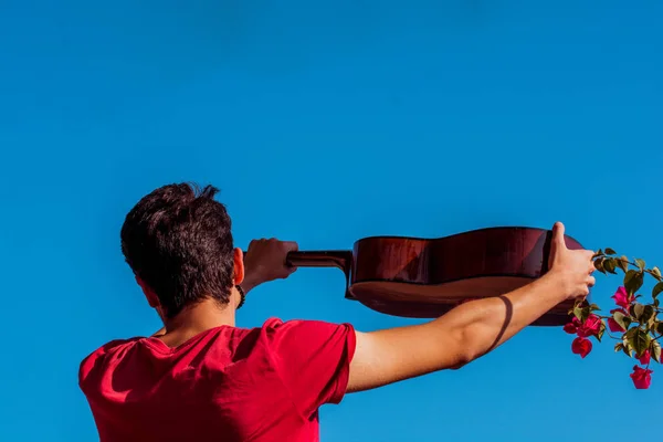 Young man rising an accoustic guitar in the sky