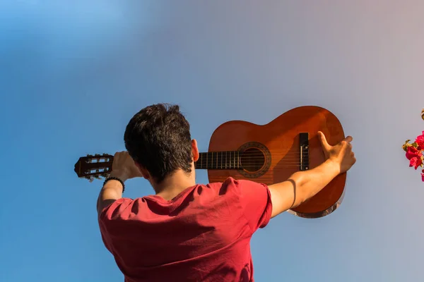 Young man rising an accoustic guitar in the sky