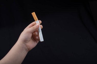 Siyah arka planda elinde sigara tutan bir çocuk..
