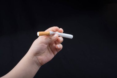 Siyah arka planda elinde sigara tutan bir çocuk..