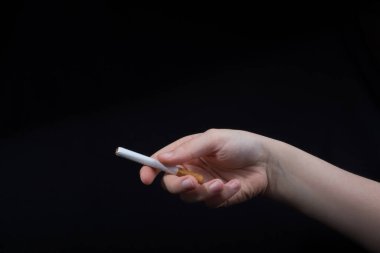 El siyah arka planda bir sigara tutuyor.