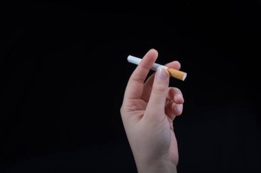 El siyah arka planda bir sigara tutuyor.