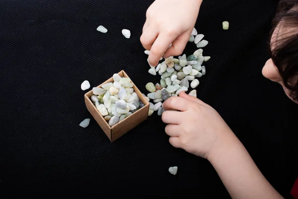 El, kutuyu taş çakıl taşlarıyla dolduruyor. Siyah arka planda çakıl taşları.