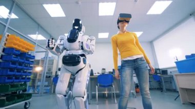 İnsan benzeri robot ve sanal gözlüklü genç bir kadın dans ediyor.